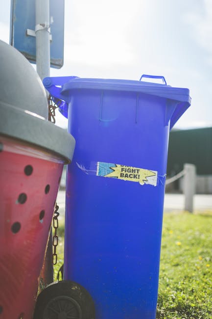Close-up image of a pile of crushed and crumpled aluminium cans and plastic bottles, with visible labels and metallic finishes. The cans and bottles vary in colour, including silver, red, blue, black,